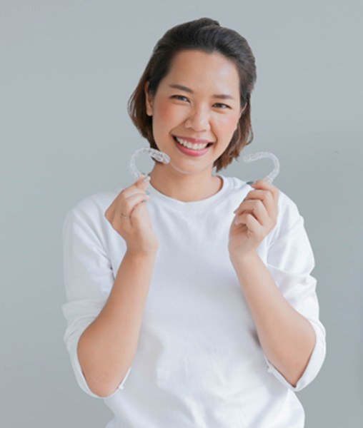 Woman in white shirt smiling while holding Invisalign aligners