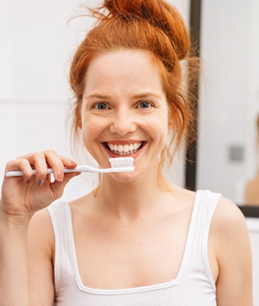 Happy red-haired woman in white shirt holding toothbrush