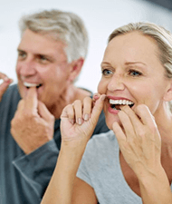 a couple flossing their teeth to avoid dental emergencies