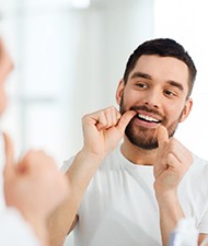 Man in white shirt flossing to care for his dental implants