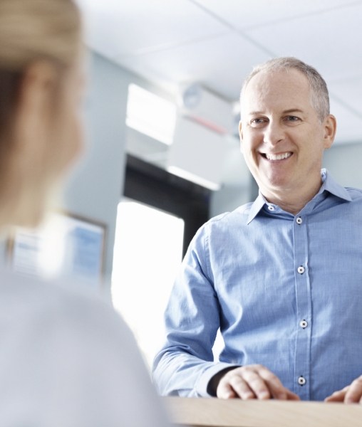 Older man checking in at front dental office for dental implant tooth replacement