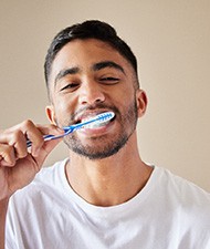 Man in white shirt smiling while brushing teeth
