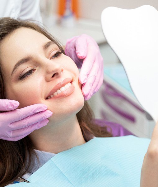 a woman smiling while looking into a handheld mirror