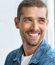 Man in denim jacket standing next to window and smiling