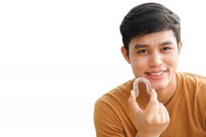 young man smiling and holding Invisalign aligner